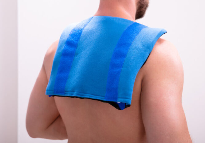 Rear View Of A Shirtless Man With Blue Ice Pack On His Shoulders And Back